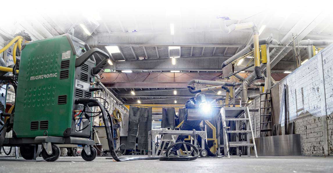 Welder at work in a fabrication workshop beside a Migatronic machine